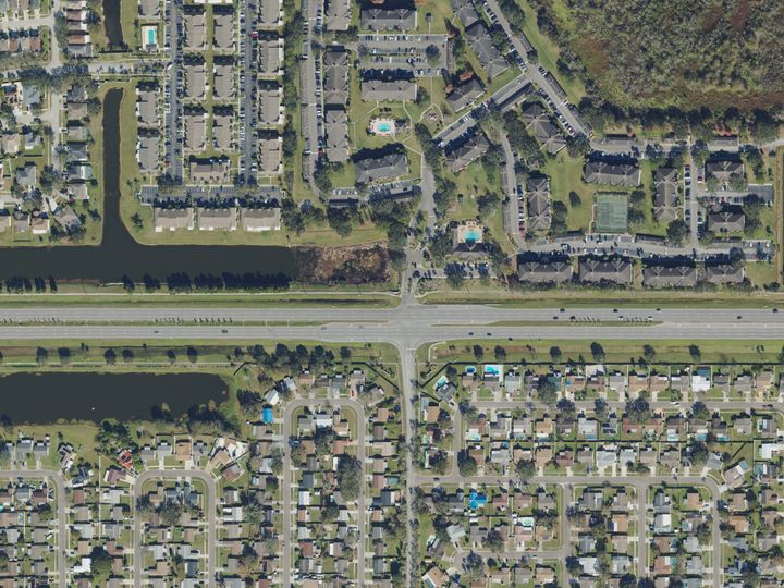 Apartment buildings around their parking lots on one side of a wide road in Brandon, and streets of single-family houses on the other, seen from above
