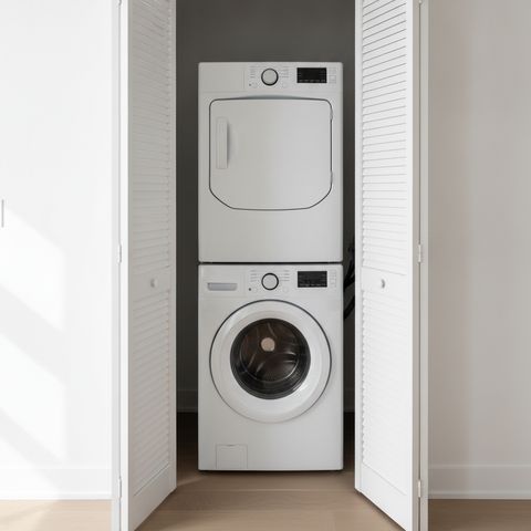 A washer and dryer stacked in a hallway closet, its white louvered doors folded open
