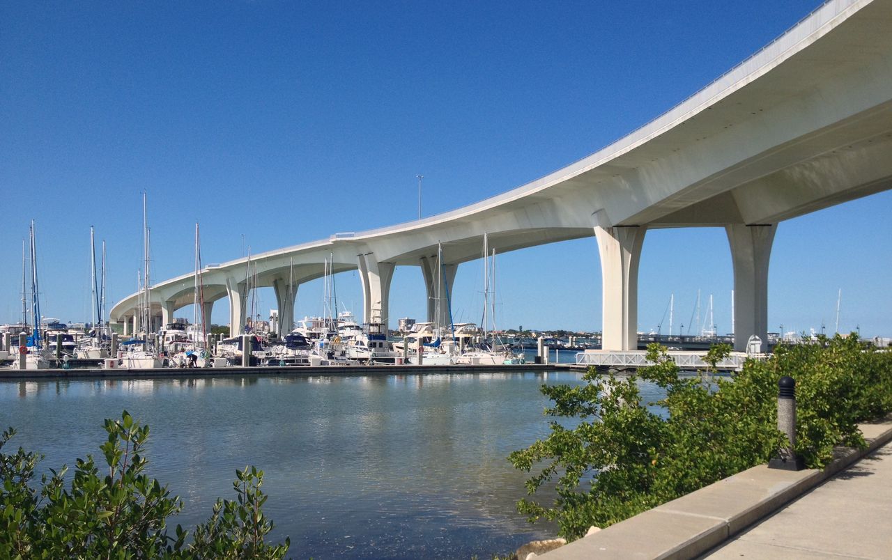 The high white span of the Memorial Causeway bridge curving over a marina of sailboats, mangroves and a waterside walk in front