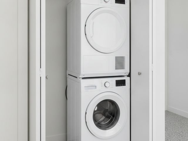 A compact dryer stacked on a front-load washer in a hallway closet, the closet doors open