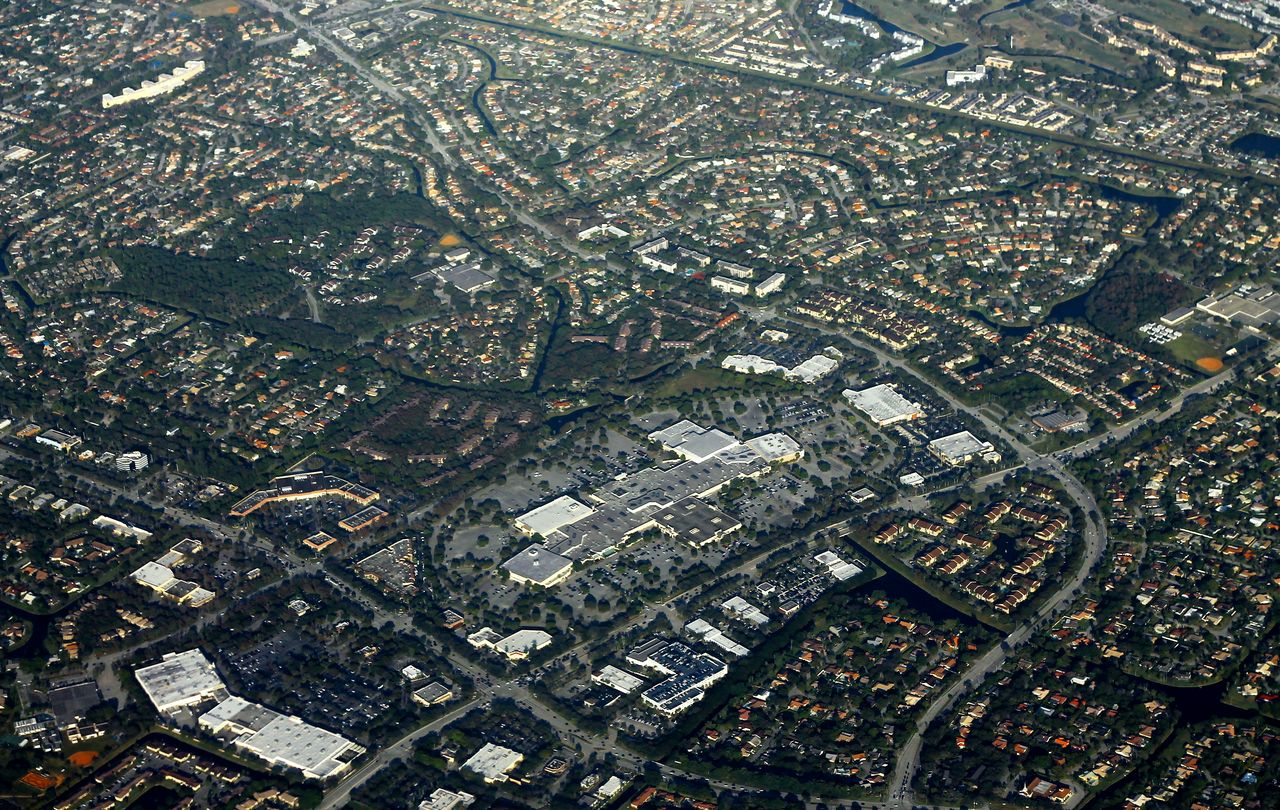 Aerial view of tile-roof houses on curving streets, canals, low-rise condo buildings and the Coral Square mall