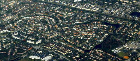 Curving streets of tile-roof houses, a looping canal and low-rise condo blocks, seen from the air