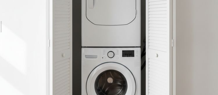 White louvered closet doors folded open around a stacked washer and dryer