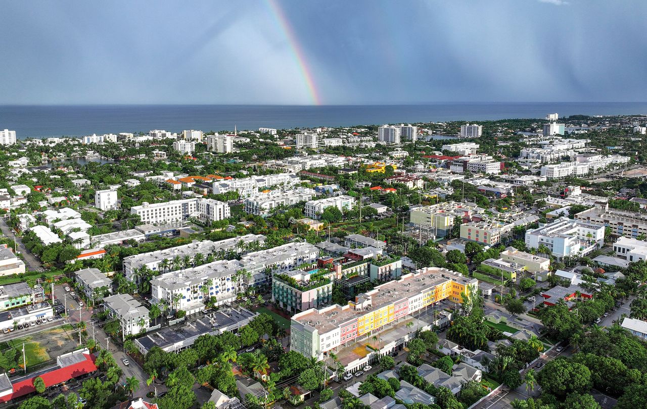 Aerial view of Delray Beach: low and mid-rise buildings among trees, condo buildings along the shore and a rainbow over the ocean
