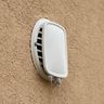 A dryer vent hood on a stucco wall, its flap shut with lint caught at the edge