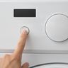 A fingertip pressing a round button on a dryer’s plain control panel