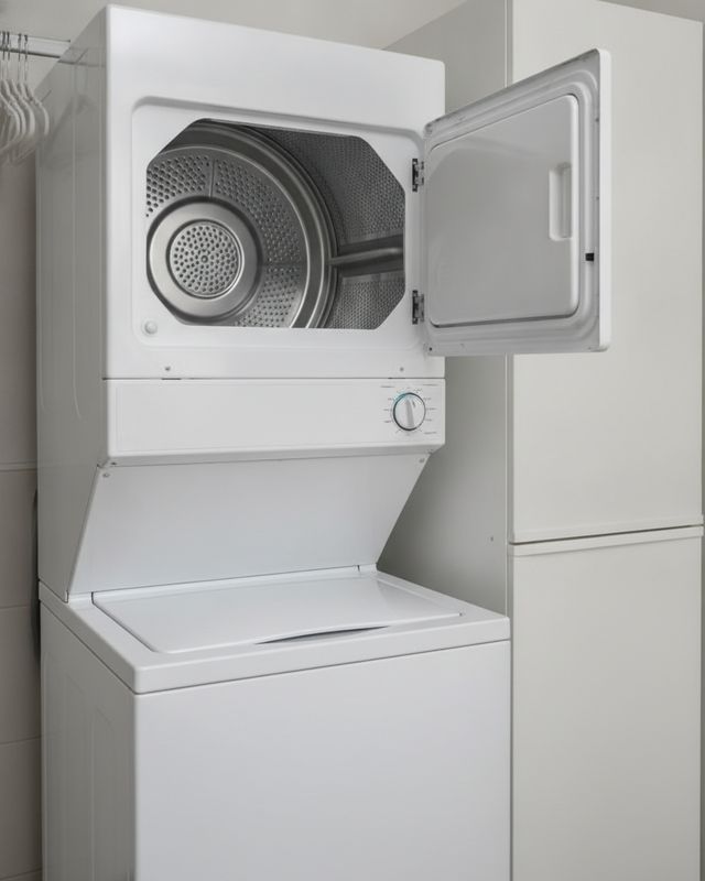 A tall white laundry center with its upper dryer door open above a top-loading washer