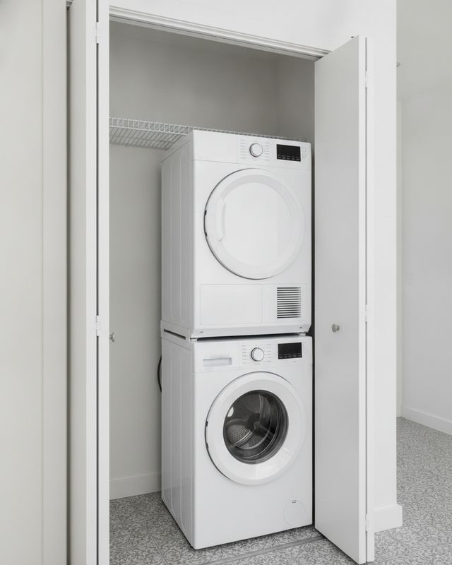 A compact dryer stacked on a front-load washer in a hallway closet, the closet doors open