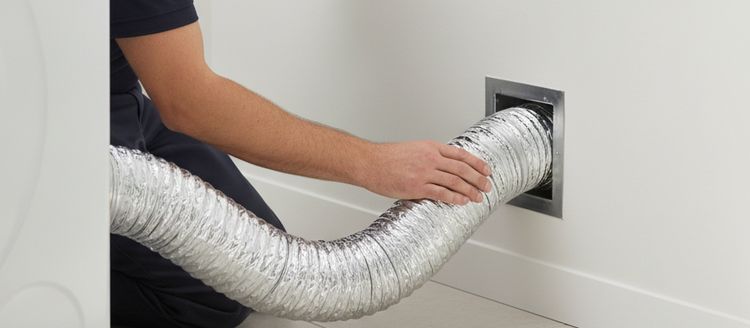 A technician’s hand on the dryer duct where it enters the wall opening
