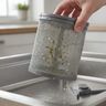 A hand lifting a mesh dishwasher filter with food bits clinging to it