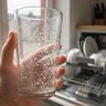 A hand holding up a drinking glass covered in white spots and film