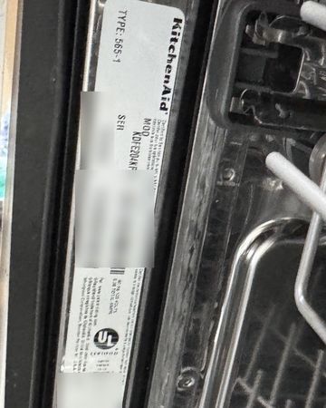 The model and serial label on the tub frame inside a KitchenAid dishwasher, beside the racks