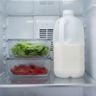 Food containers and a milk jug pushed up against the air vent at the back of a refrigerator