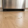 A puddle of water on a wood floor in front of a refrigerator