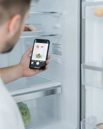 A hand holding a phone to photograph the model and serial sticker inside a refrigerator