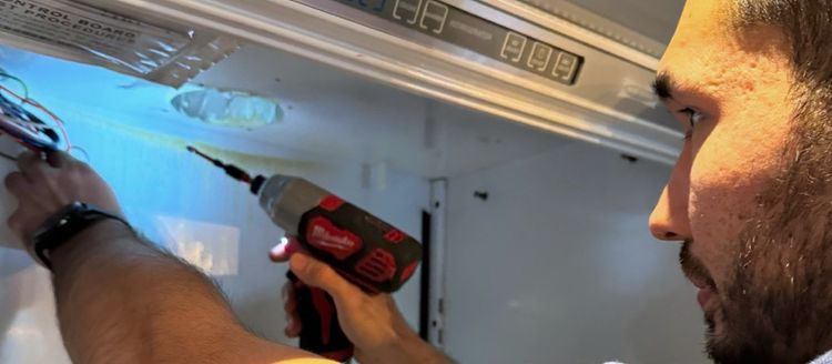 A technician with a cordless driver at the control housing inside a refrigerator