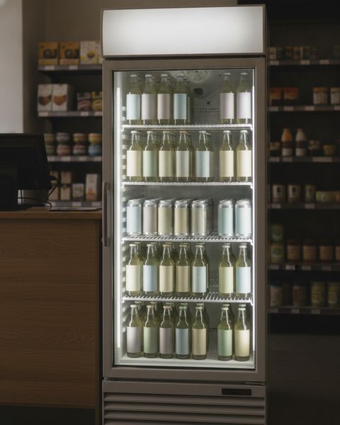 A glass-door drink cooler full of bottles and cans beside a small store’s checkout counter