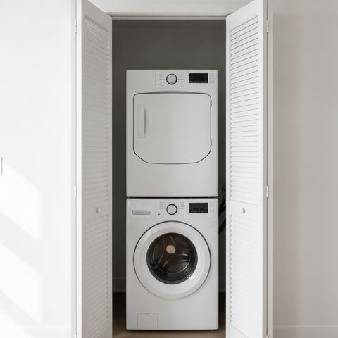 White louvered closet doors folded open around a washer with a dryer stacked on top