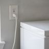 A freezer’s power cord plugged into a wall outlet behind the cabinet