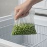 A hand holding a soft, dripping bag of frozen peas over a freezer basket