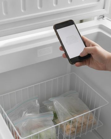 A hand holding a phone to photograph the model label inside an open chest freezer