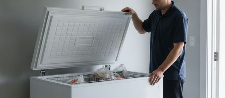 A technician’s hands on the raised lid and the rim of an open chest freezer