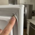 A fingertip on the corner of a refrigerator door gasket that has split