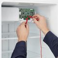 A technician’s hands holding multimeter probes to the control board of a refrigerator