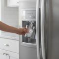 A hand holding a glass to the water and ice dispenser in a stainless refrigerator door