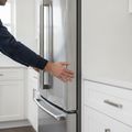 A hand on the door of a new stainless refrigerator, its trim still under clear protective film
