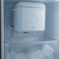A refrigerator ice maker encased in ice, icicles hanging into the bin