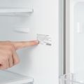 A fingertip under one line of the model and serial label on the inside wall of a refrigerator
