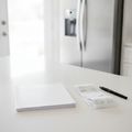 An owner’s manual and a store receipt on a white kitchen counter, a stainless French door refrigerator behind them