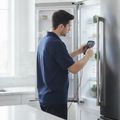 A technician in a navy polo testing an open refrigerator with a multimeter