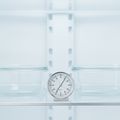 A dial appliance thermometer standing on a glass shelf inside a white built-in refrigerator