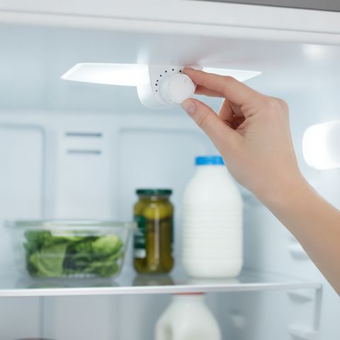 A hand turning the temperature dial inside an open refrigerator