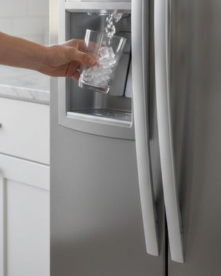 A hand holding a glass under a refrigerator door dispenser as ice drops into it