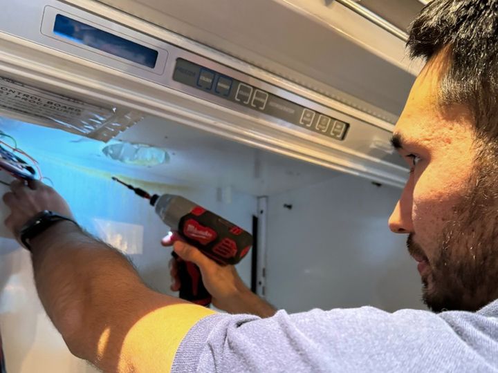 Technician using a cordless driver on the control housing of a built-in refrigerator