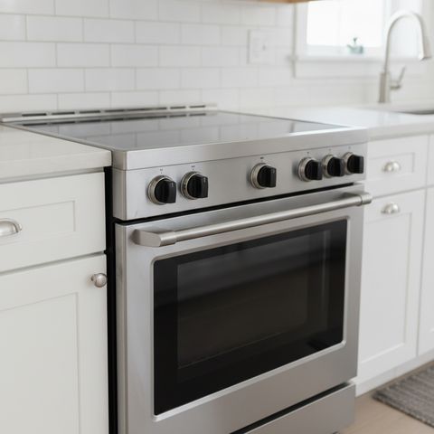A stainless steel electric range with front control knobs and a smooth glass top, between white cabinets