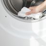 A hand wiping the inside of a dryer’s door opening with a soft white cloth
