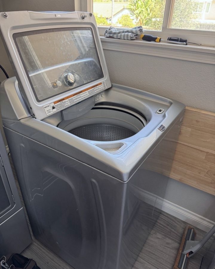 A top-load washer with its lid raised beside a window, screwdrivers on the sill, on a Beaver Appliance job
