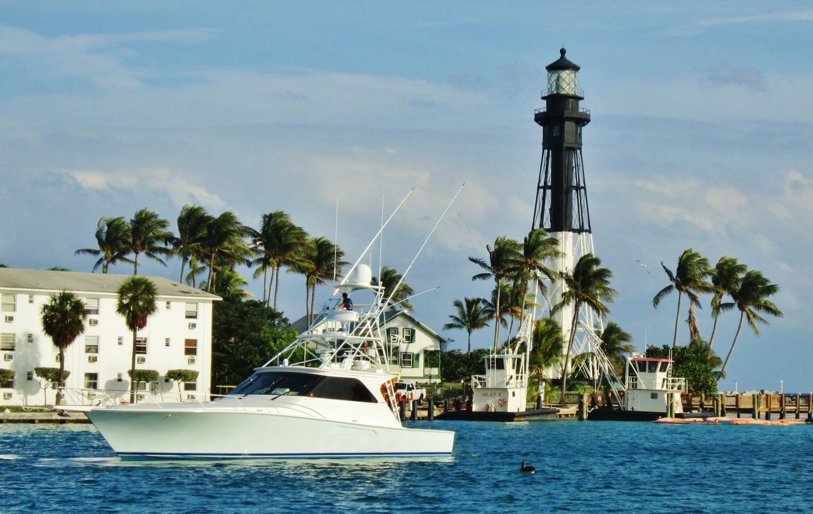 A sport-fishing boat heading through the Hillsboro Inlet past palms and the Hillsboro Inlet Light, the lighthouse in Hillsboro Beach that Lighthouse Point is named for