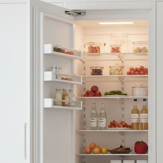 A white panel-ready built-in column refrigerator standing open, its shelves stocked