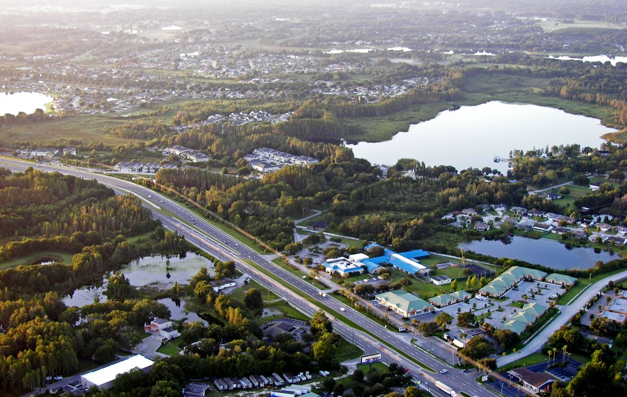 Aerial view of State Road 54 curving past lakes, woods, low offices and subdivisions in Land O’ Lakes