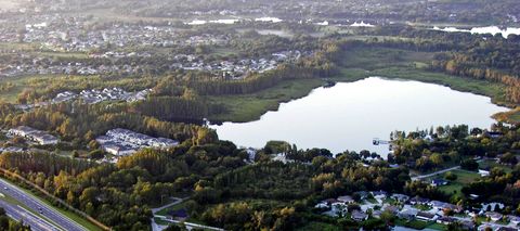 A lake ringed by woods and subdivisions beside State Road 54, seen from the air