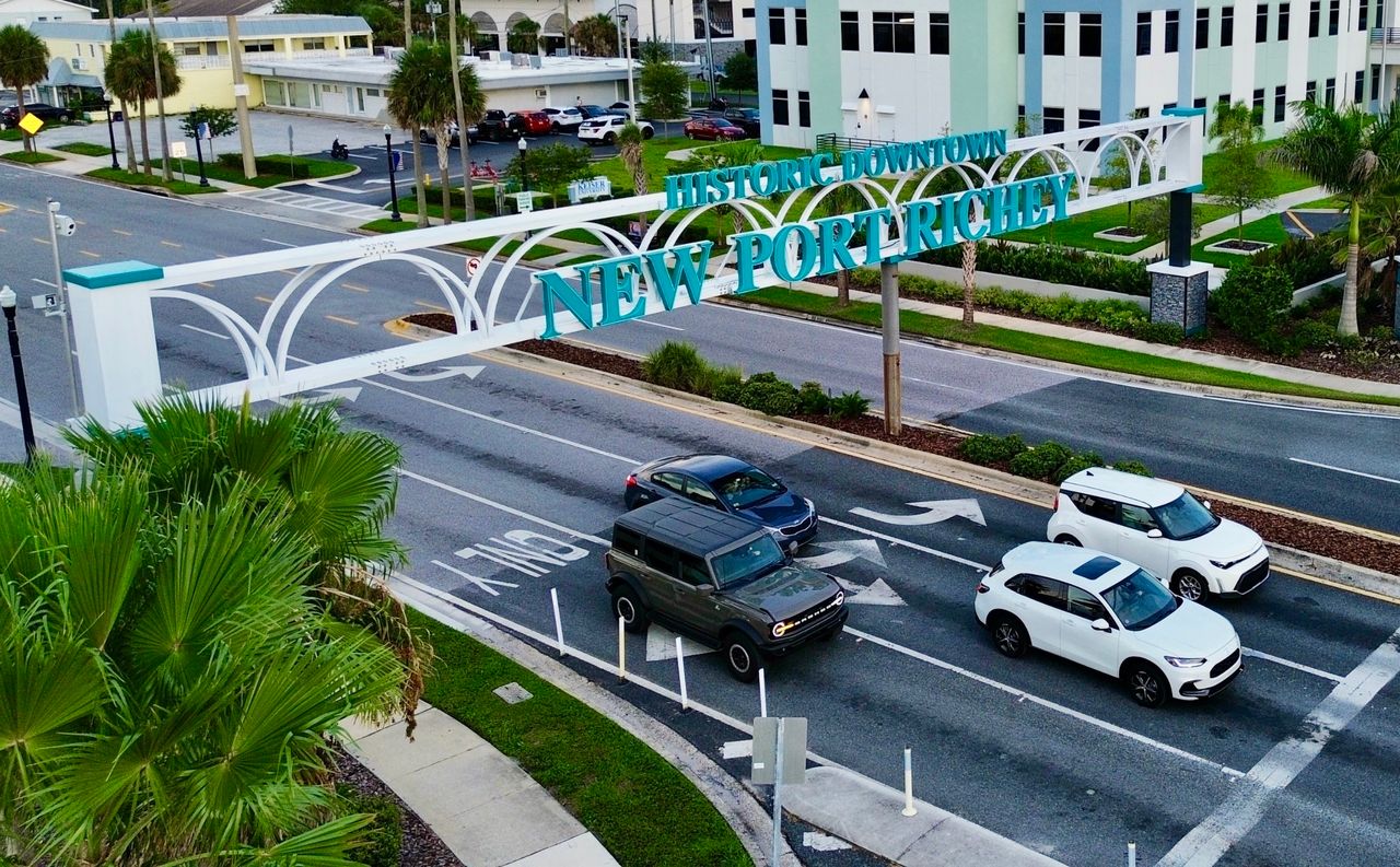 The Historic Downtown New Port Richey arch over Main Street, seen from above, palms beside the road and cars passing under it