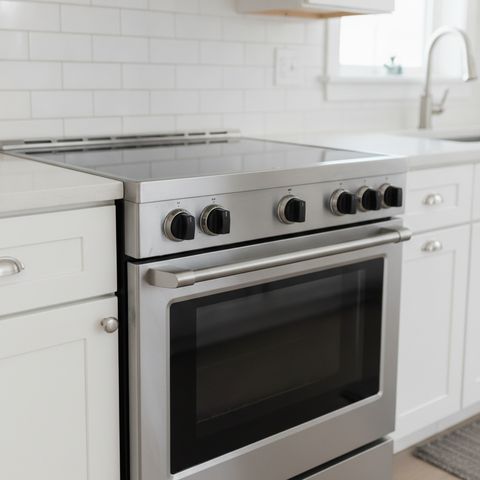 A stainless steel slide-in range with a smooth black glass top, between white cabinets