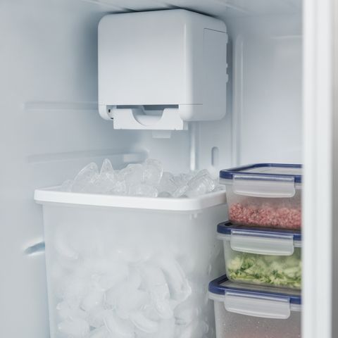 An ice maker high in a refrigerator’s freezer above a bin of crescent ice cubes