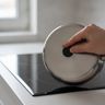 A hand holding a magnet to the bottom of a stainless steel saucepan