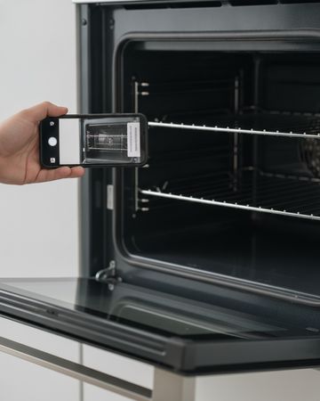 A hand holding a phone to photograph the label on the frame of an open oven